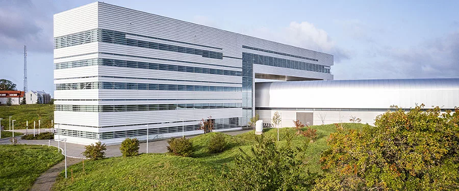 Image of the external MAX IV building with a focus on the office building, trees and green hills in the surroundings.
