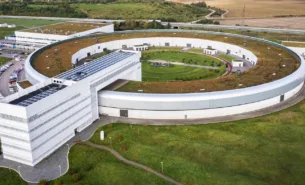 Drone image of MAX IV from above, surrounded by green landscape and the horizon.