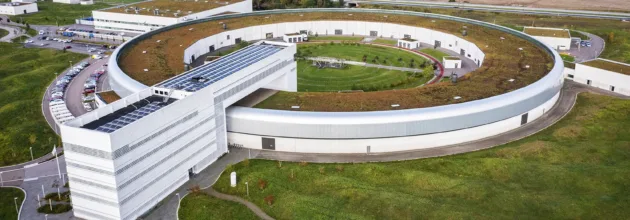 Drone image of MAX IV from above, surrounded by green landscape and the horizon.